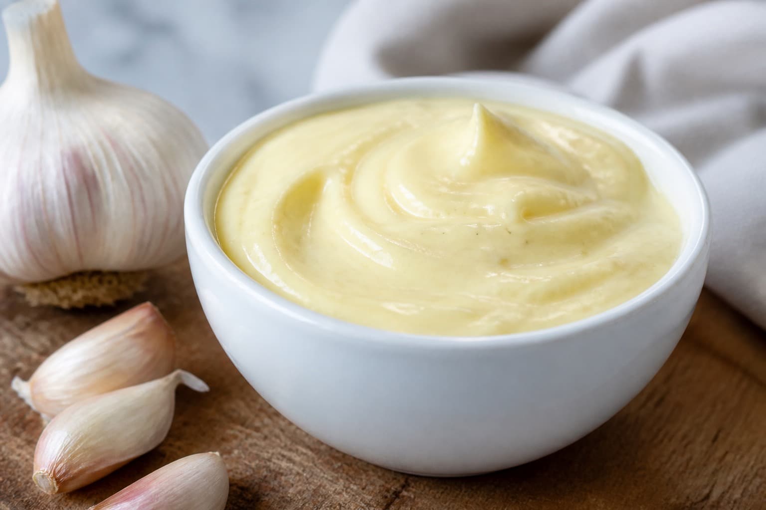 Skål med gul aioli og hvidløgsfed ved siden af